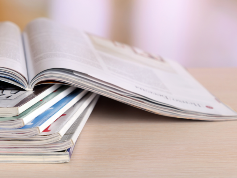 Stack of open and closed magazines on a light wooden surface with blurred background.