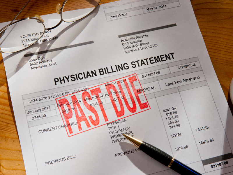 Physician billing statement with "PAST DUE" stamp, eyeglasses, and pen on wooden table.