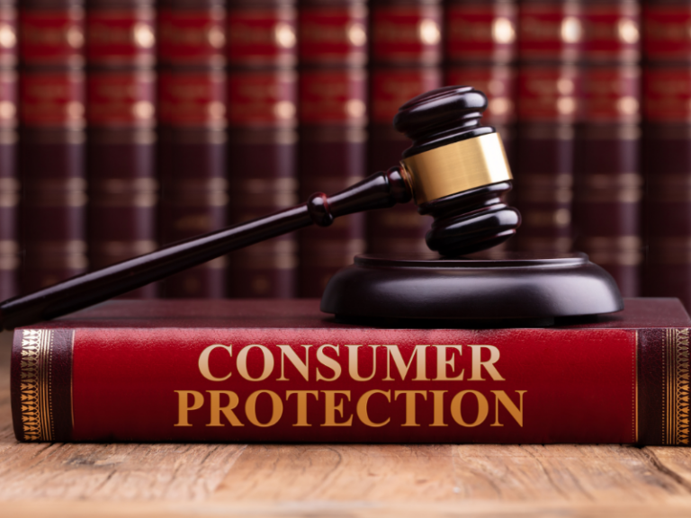 Close-up of a wooden judge’s gavel resting on a red book titled "Consumer Protection" with law books in the background.