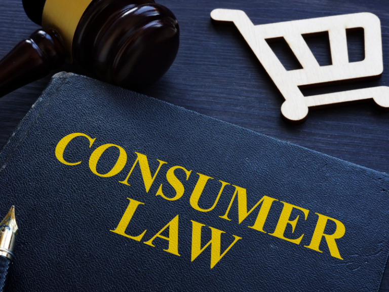Close-up of a black book titled "Consumer Law" in yellow text, with a wooden gavel and shopping cart icon on a dark surface.