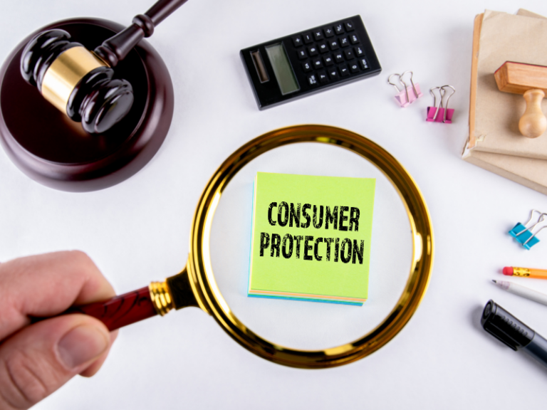 Magnifying glass focusing on green note with "Consumer Protection" text, surrounded by gavel, calculator, and office supplies.
