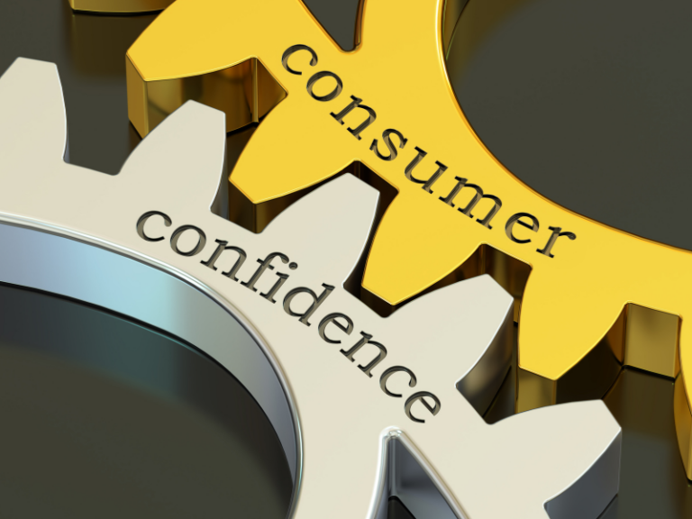 Close-up of interlocking gold and silver gears labeled "consumer" and "confidence" on a dark background.