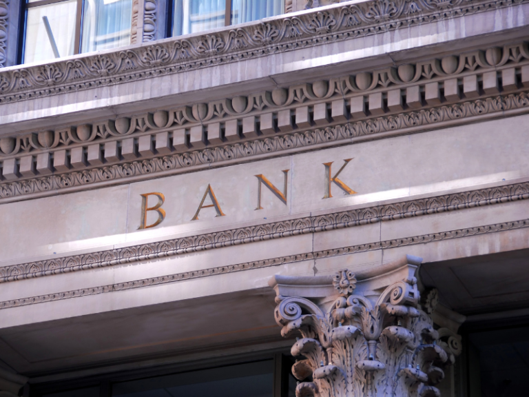 Ornate stone bank building facade with gold lettering and Corinthian column detail.