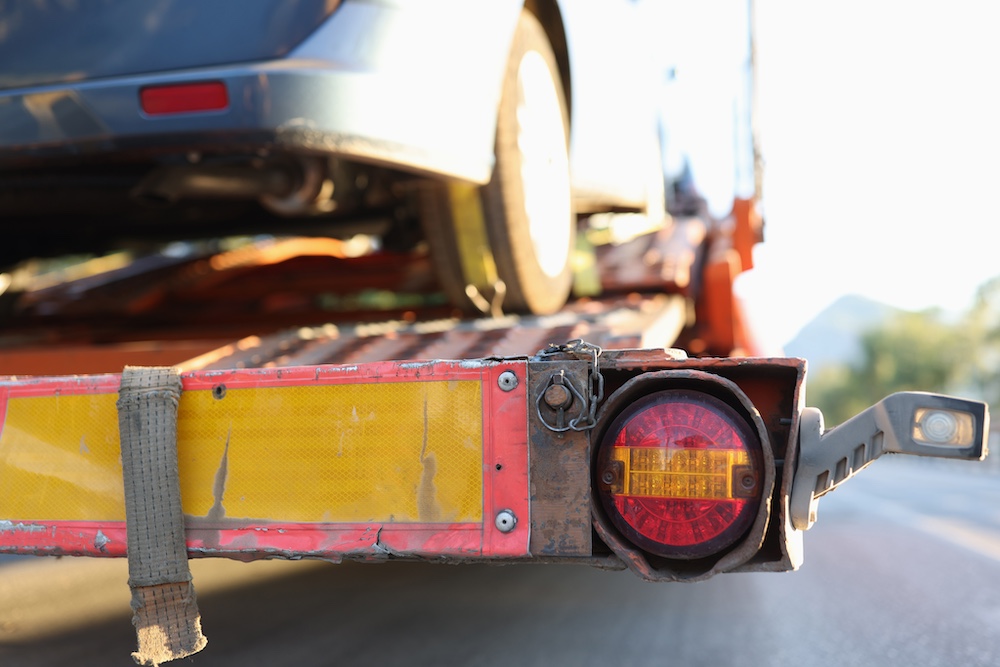 Close-up view of the rear section of a red vehicle transport trailer with a blue car loaded, highlighting the taillight and yellow reflective strip.