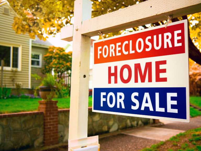 Foreclosure home for sale sign in front of suburban house with autumn foliage.