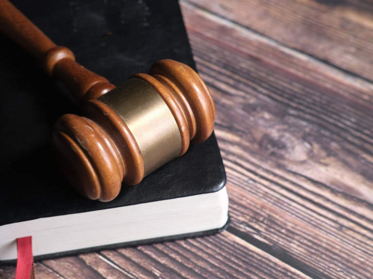 Wooden judge's gavel resting on a black hardcover book with a red ribbon marker.