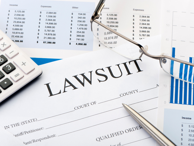 Document titled "Lawsuit" with financial charts, a calculator, eyeglasses, and a pen on a desk.