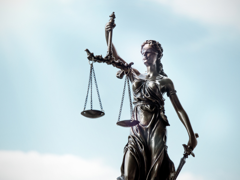 Bronze statue of Lady Justice blindfolded, holding scales and a sword against a blue sky.