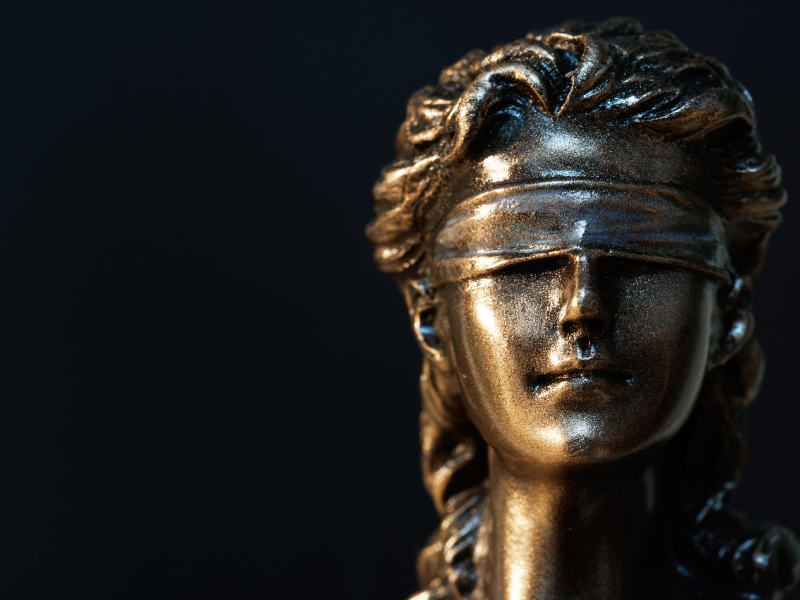 Close-up of a bronze statue of Lady Justice with a blindfold against a dark background.