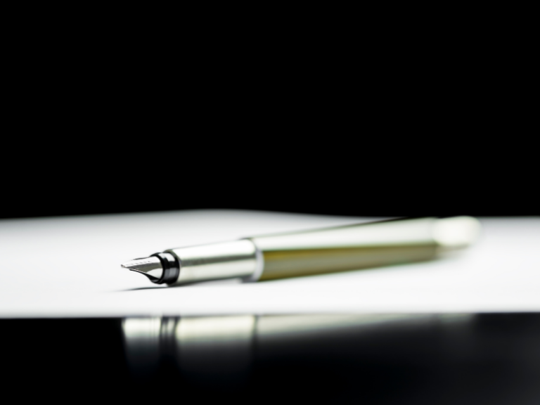 Close-up of a silver fountain pen resting on a white surface with a black background.
