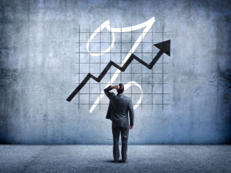 Man in suit looking at rising arrow chart and large percentage symbol on wall.
