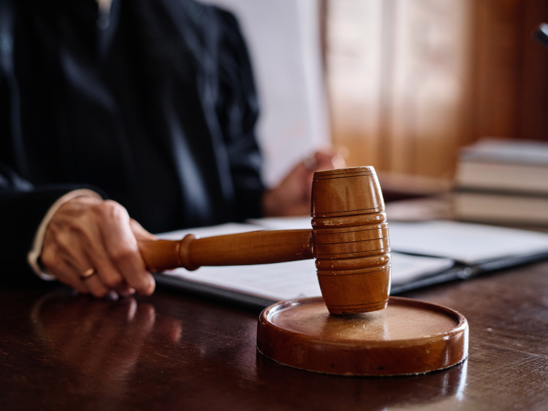 Close-up of a wooden judge's gavel held by a person in a black robe, with legal documents on a desk.