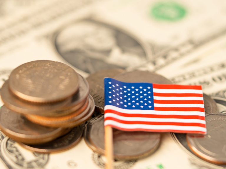 Small American flag placed on scattered U.S. coins and dollar bills background.