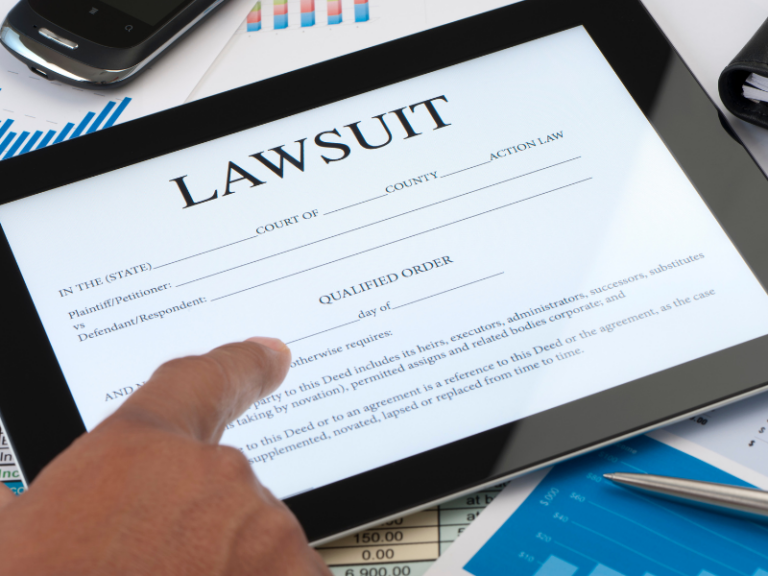 Finger pointing at a digital tablet displaying a lawsuit document, surrounded by charts and a smartphone.