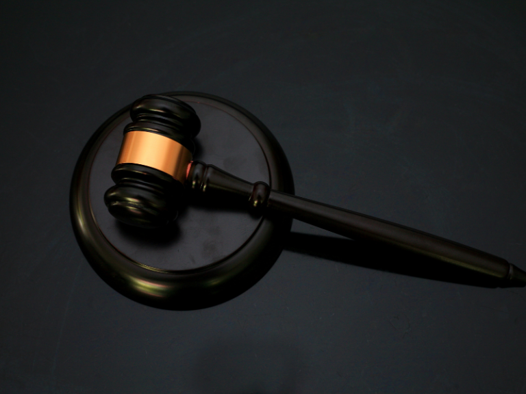 Dark wooden judge's gavel with a gold band resting on a matching sound block.