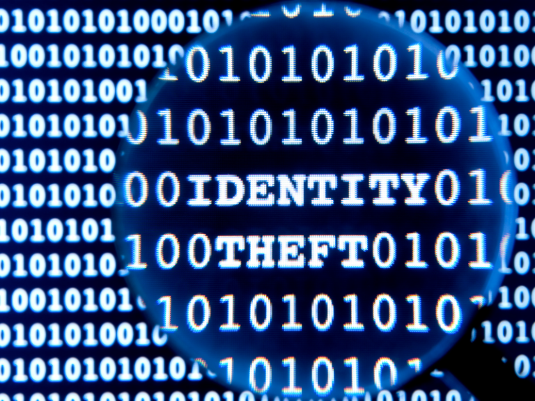 Close-up of binary code with words "IDENTITY THEFT" highlighted under a magnifying glass.