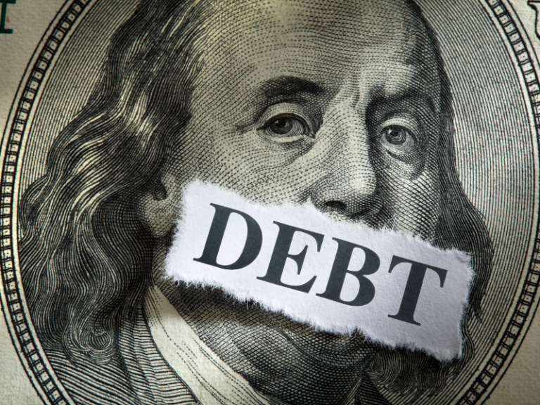 Close-up of Benjamin Franklin's portrait on a US hundred-dollar bill with a torn paper labeled "DEBT" covering his mouth.