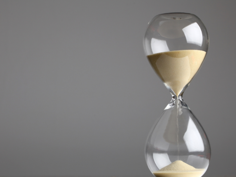 Transparent hourglass with beige sand flowing against a plain gray background.