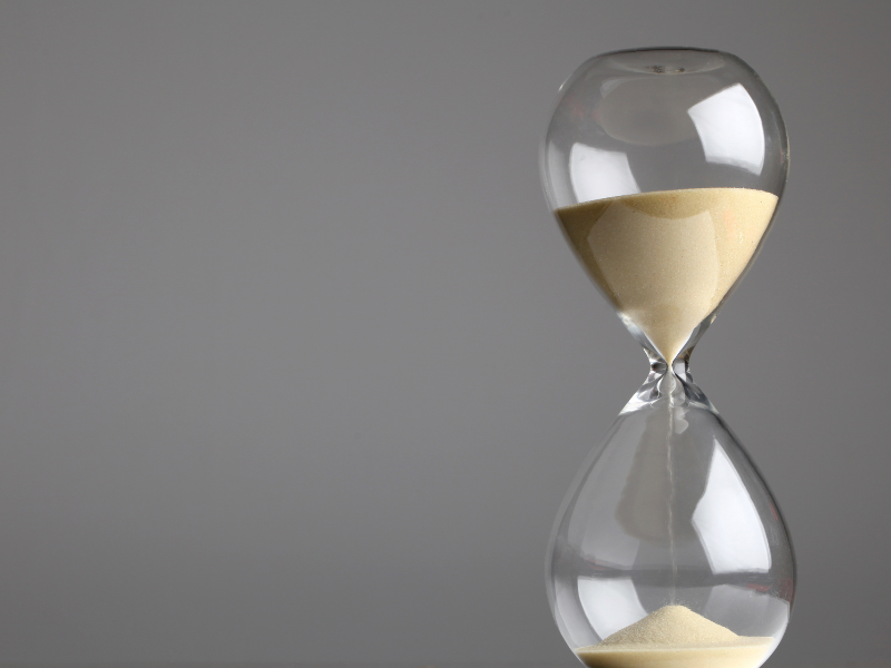 Transparent hourglass with beige sand flowing against a plain gray background.