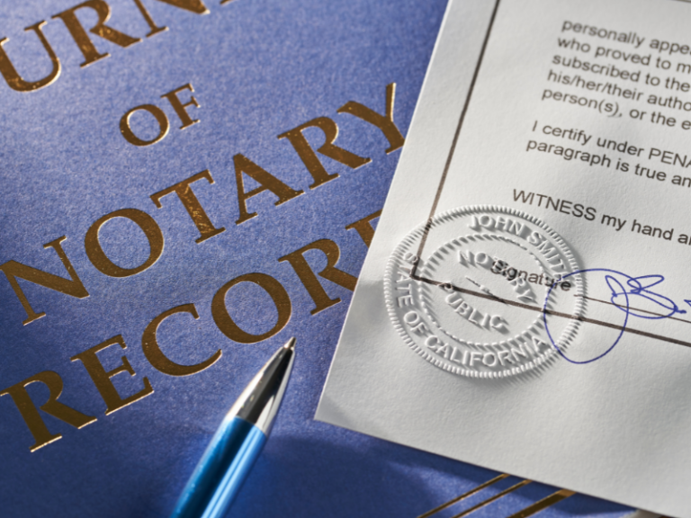 Close-up of a notary record book, a signed document with a California notary seal, and a blue pen.