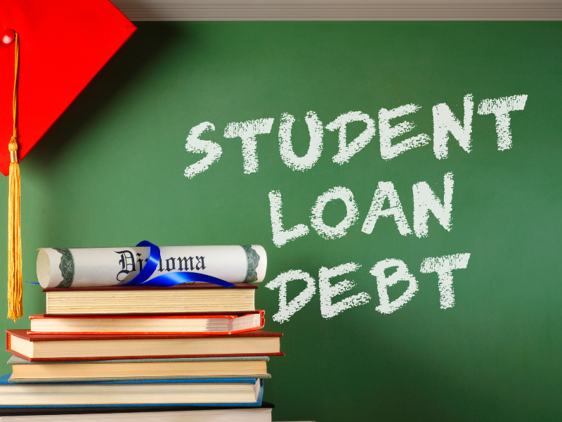 Stack of books with diploma and red graduation cap beside chalkboard displaying "Student Loan Debt" text.