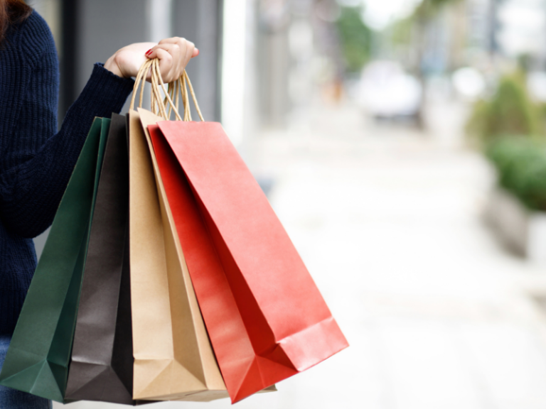 Close-up of a person holding multiple colorful paper shopping bags outdoors.