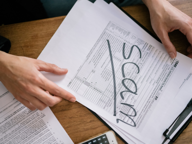 Hands holding a tax form with "SCAM" written across it in bold letters.