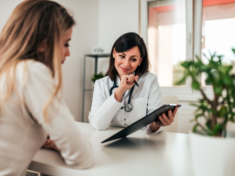 Female doctor with stethoscope reviewing documents with patient in medical office.