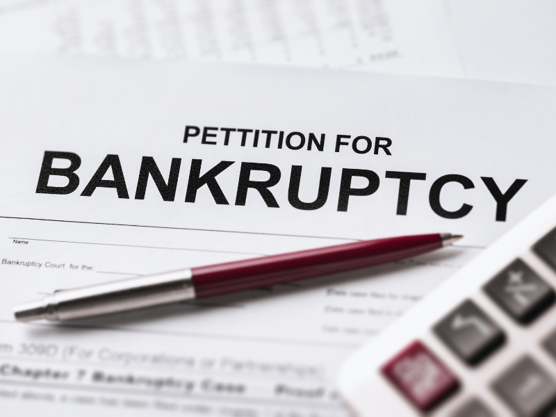 Close-up of a bankruptcy petition document with a red pen and calculator on a white surface.