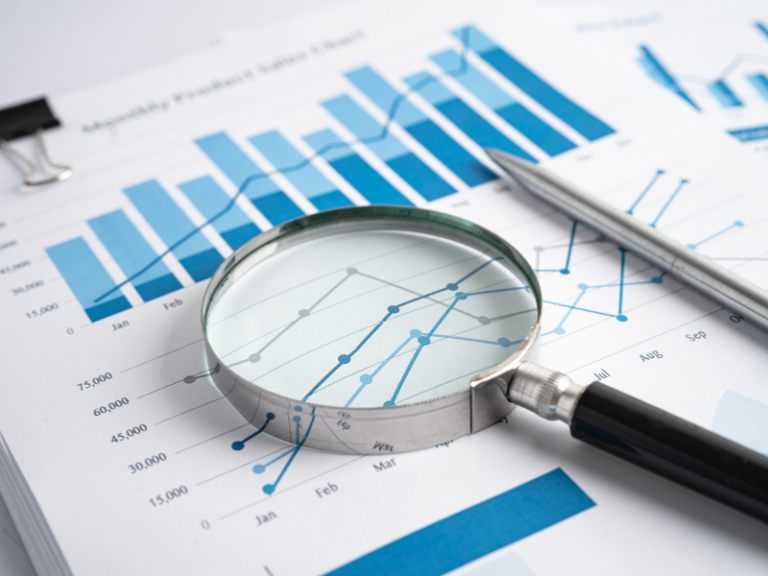 Magnifying glass and pen on financial charts with blue bar and line graphs.