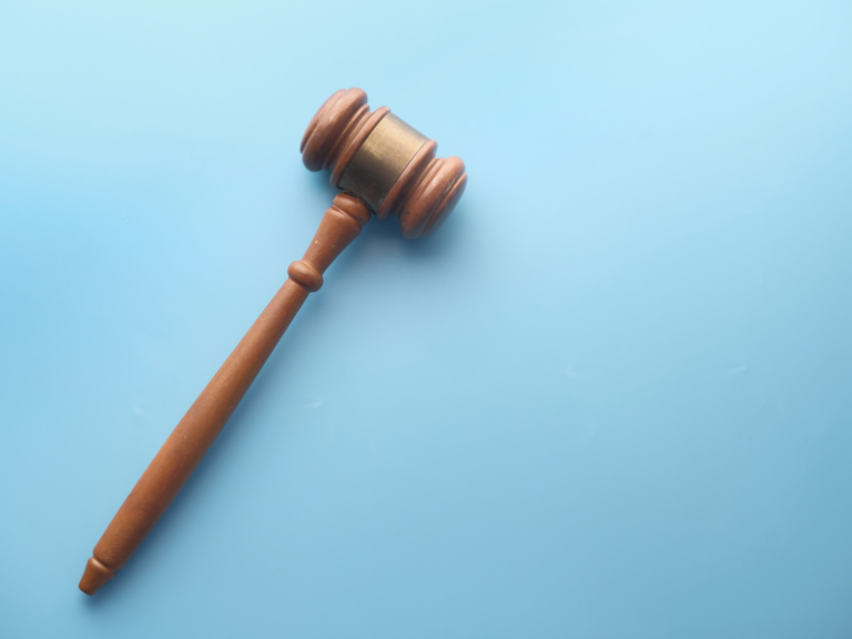 Wooden judge's gavel with brass band on light blue background.