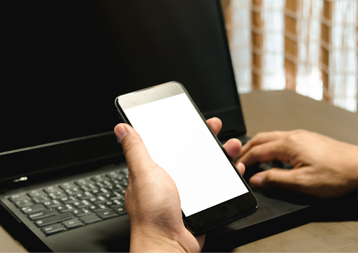 Person holding a smartphone with a blank white screen over a laptop keyboard.