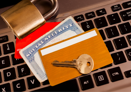 Padlock, social security card, key, and credit cards placed on a laptop keyboard.