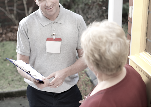 Man in gray polo with clipboard speaking to woman at residential doorway