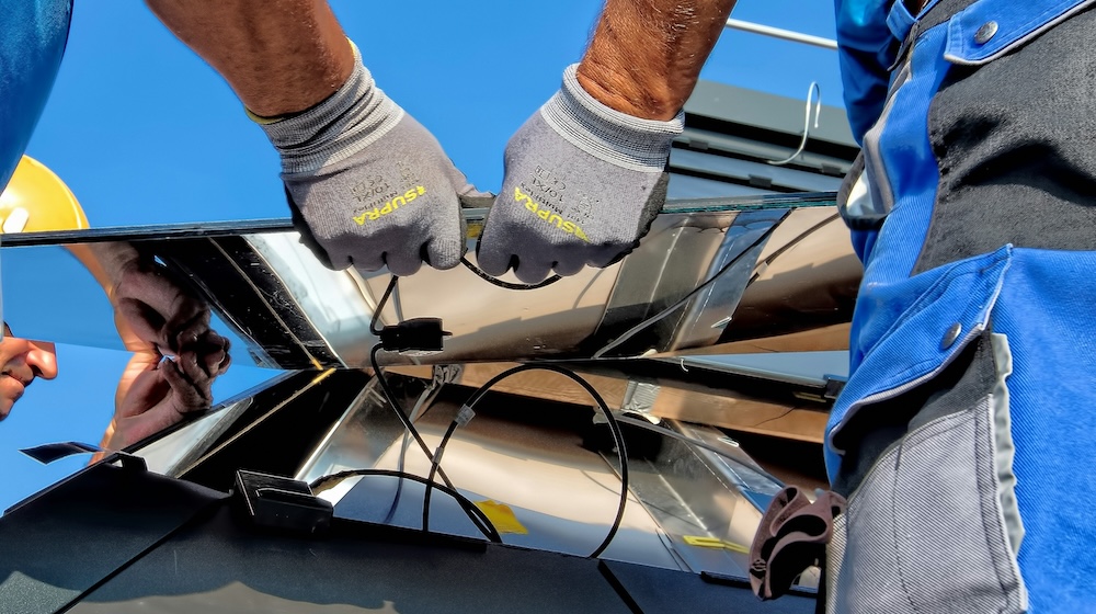 Close-up of workers' gloved hands installing or repairing reflective solar panels under clear blue sky.