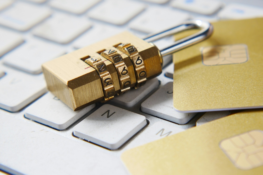 Close-up of a brass combination padlock and gold credit cards on a white computer keyboard.