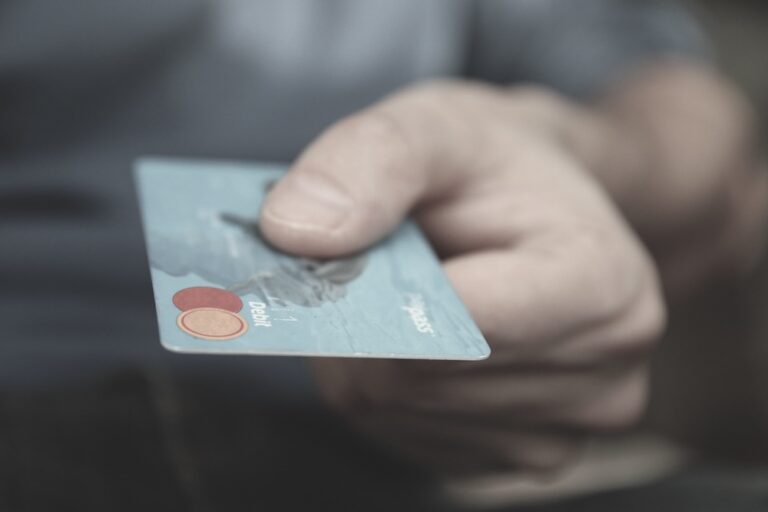 Close-up of a hand holding a light blue debit card with visible logos and text.