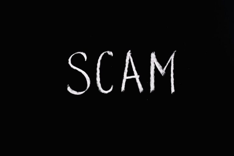 The word "SCAM" written in white chalk on a black background.