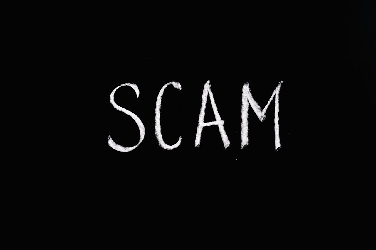 The word "SCAM" written in white chalk on a black background.