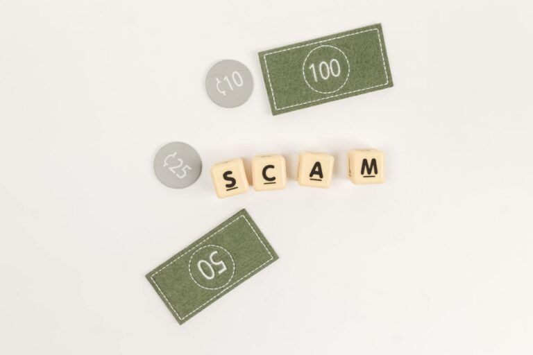 Wooden letter blocks spelling "SCAM" surrounded by play money bills and coins.