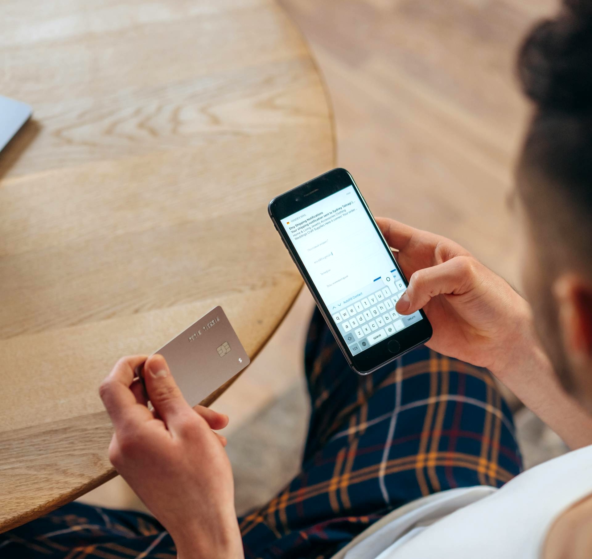 Person holding a smartphone displaying a shipping notification and a credit card over a wooden table.