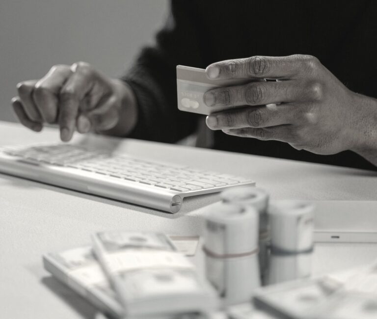 Close-up of hands holding a credit card above a white keyboard with blurred currency in the foreground.