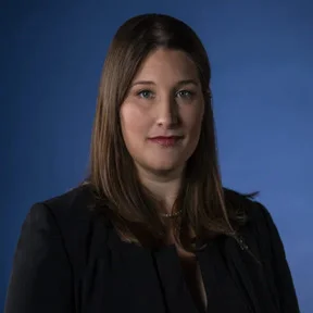 Professional portrait of a woman with long brown hair against a blue background.