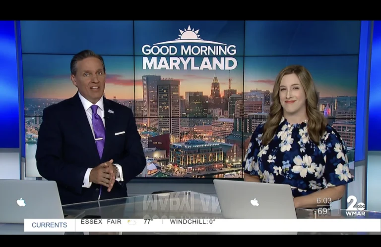 Two news anchors in professional attire presenting "Good Morning Maryland" with cityscape background on WMAR studio screen.
