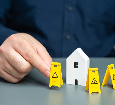 Person placing small yellow caution signs around a white miniature house model.