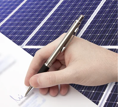 Close-up of a hand signing a document with a pen, solar panels in the background.