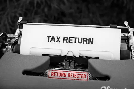 Close-up of a typewriter with a paper reading "TAX RETURN" and a red stamp "RETURN REJECTED.