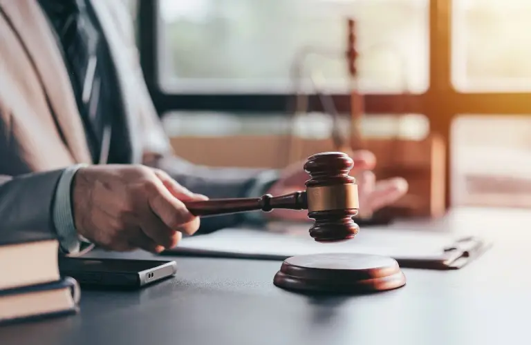 Person in a suit holding a wooden judge's gavel over a sound block on a desk.