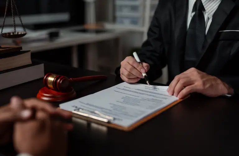 Professional in suit signing legal document at desk with gavel and scales of justice.