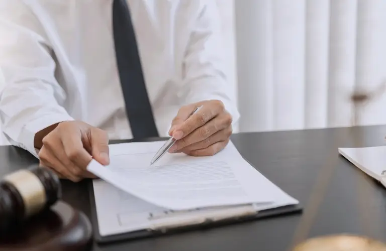 Person in white shirt and black tie reviewing documents with pen on desk.
